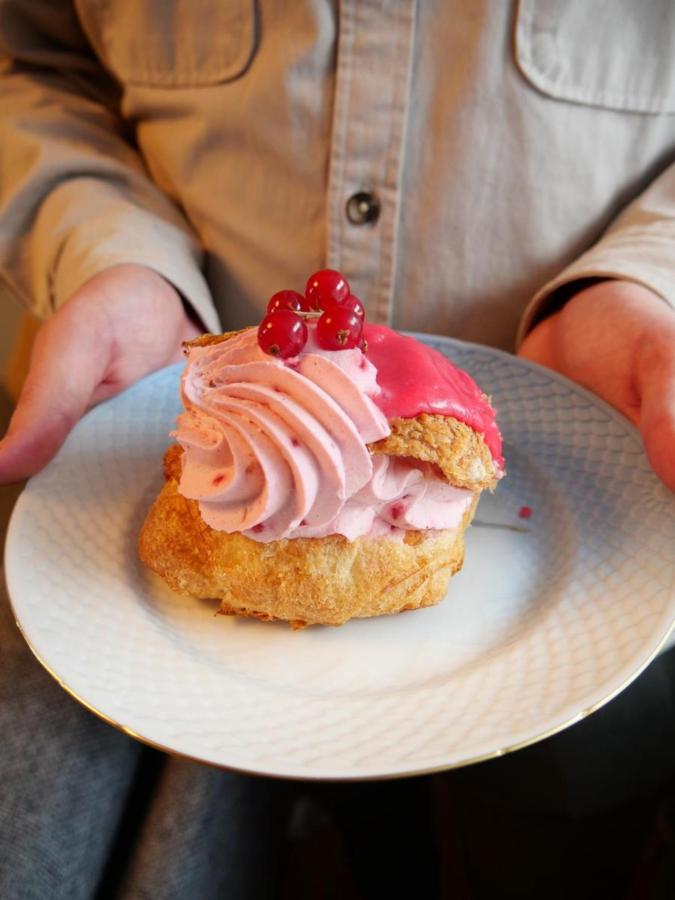 En person holder en tallerken med en fastelavnsbolle med lyserød creme og ribs på toppen.