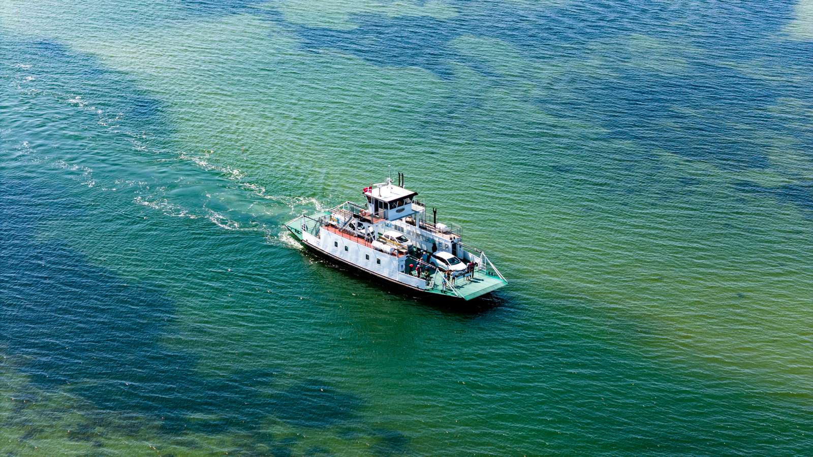 Columbus færgen sejler på åbent, grønt hav med biler og passagerer ombord set fra oven.