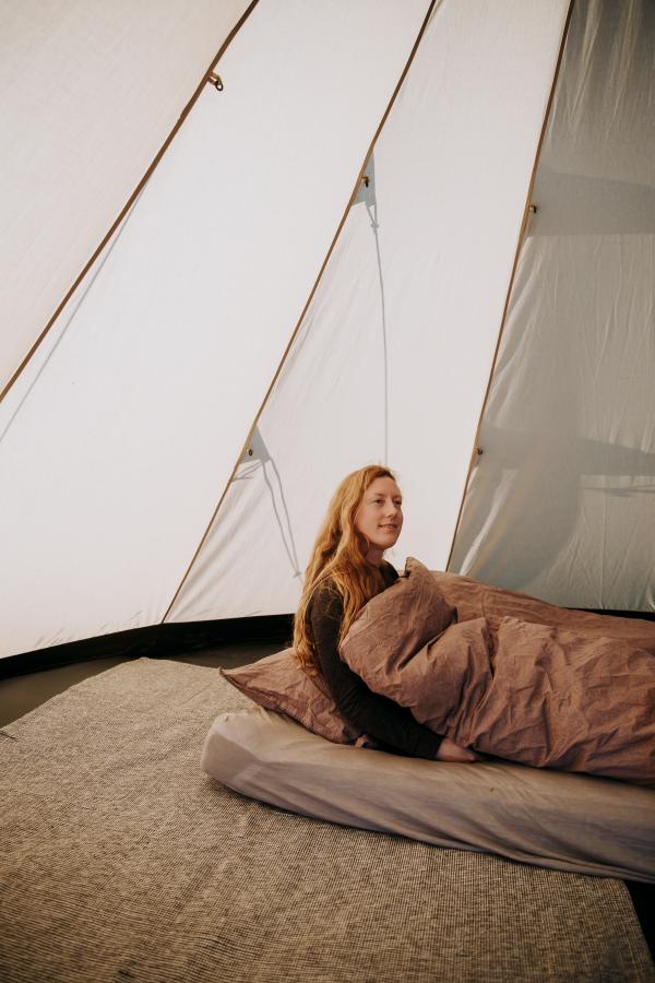 Person sidder i seng inde i glampingtelt og nyder komfortabel overnatning hos Outdoor Adventures.